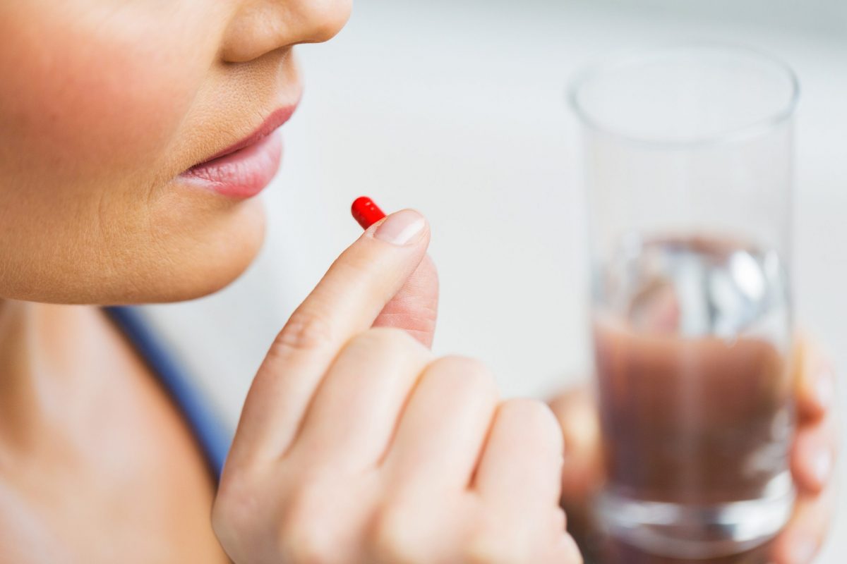 Жінка п'є таблетки для лікування гострого геморою