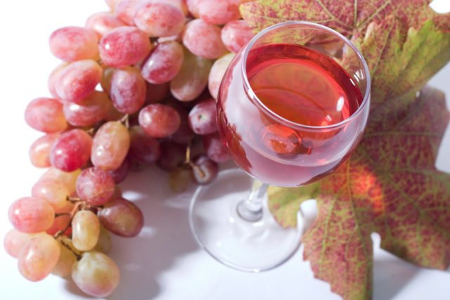 Рожеве вино в келиху і гроно винограду